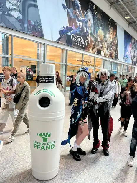 Weißer Pfandbehälter in der Messehalle der gamescom, Besucher in Kostümen daneben